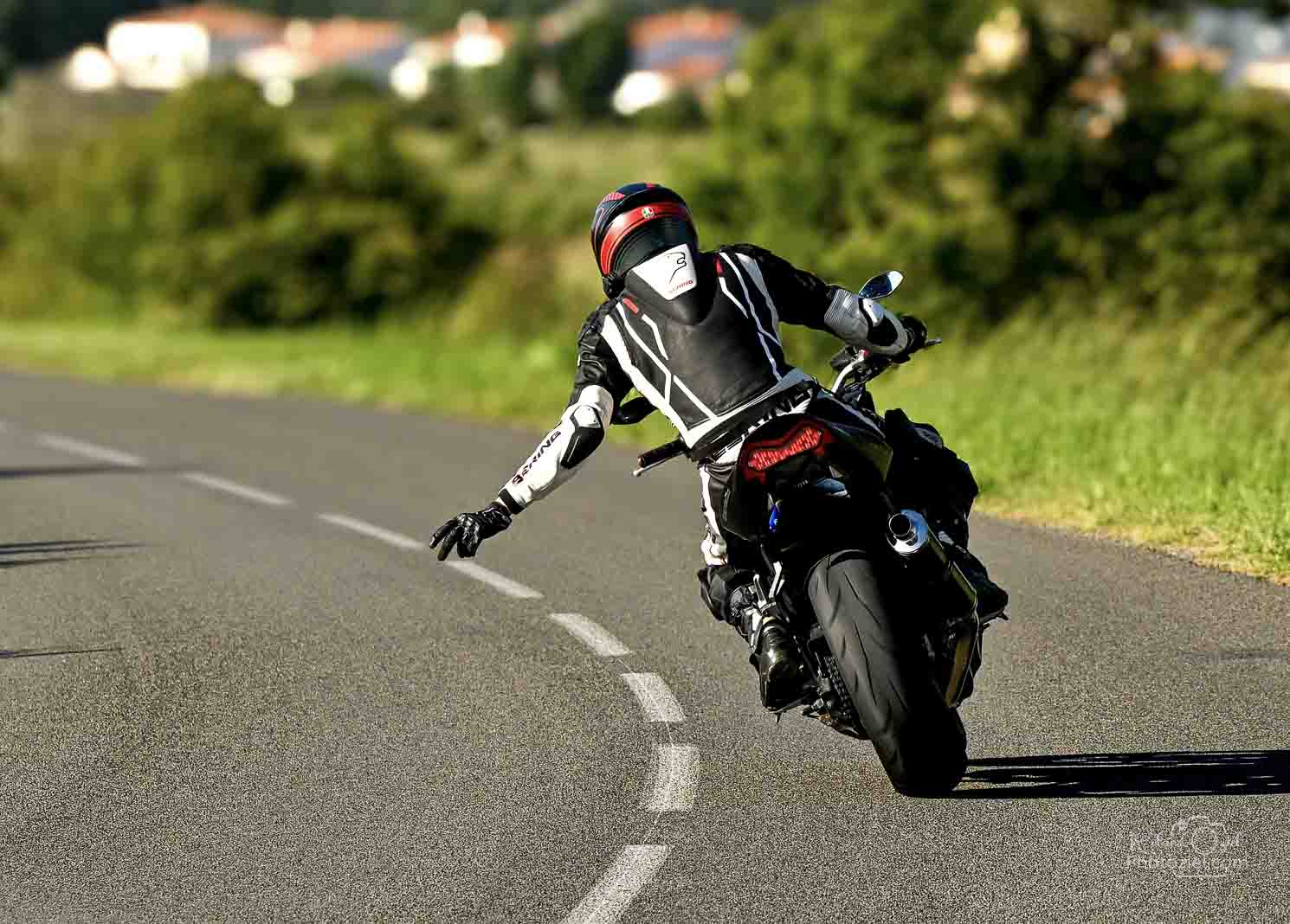 Photo de la moto par derrière avec le pilote faisant un signe  de la main