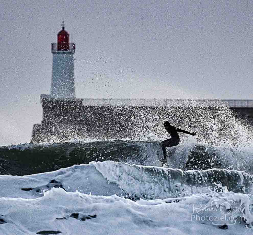 Photo d&apos;un surfeur avec de gorsses vagues devant le phare des sables d&apos;olonne